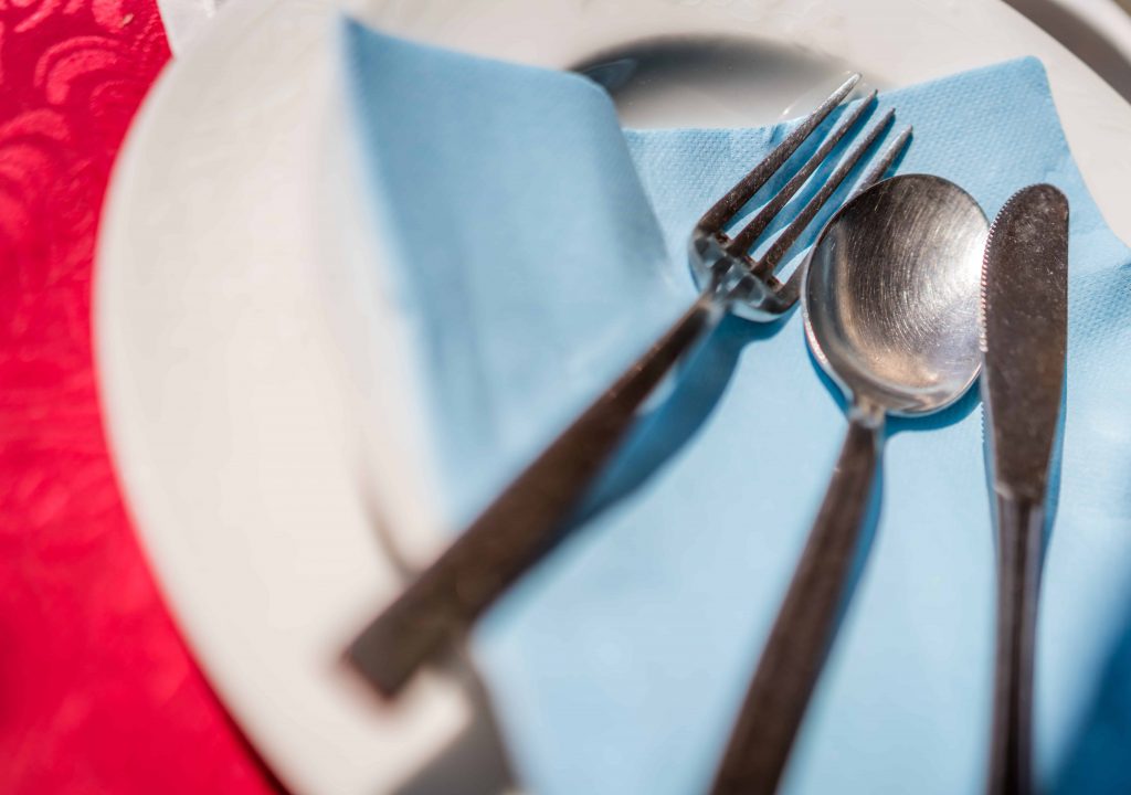 Fork, knife and spoon on a blue napkin on a plate on the table before the start of the service in the restaurant