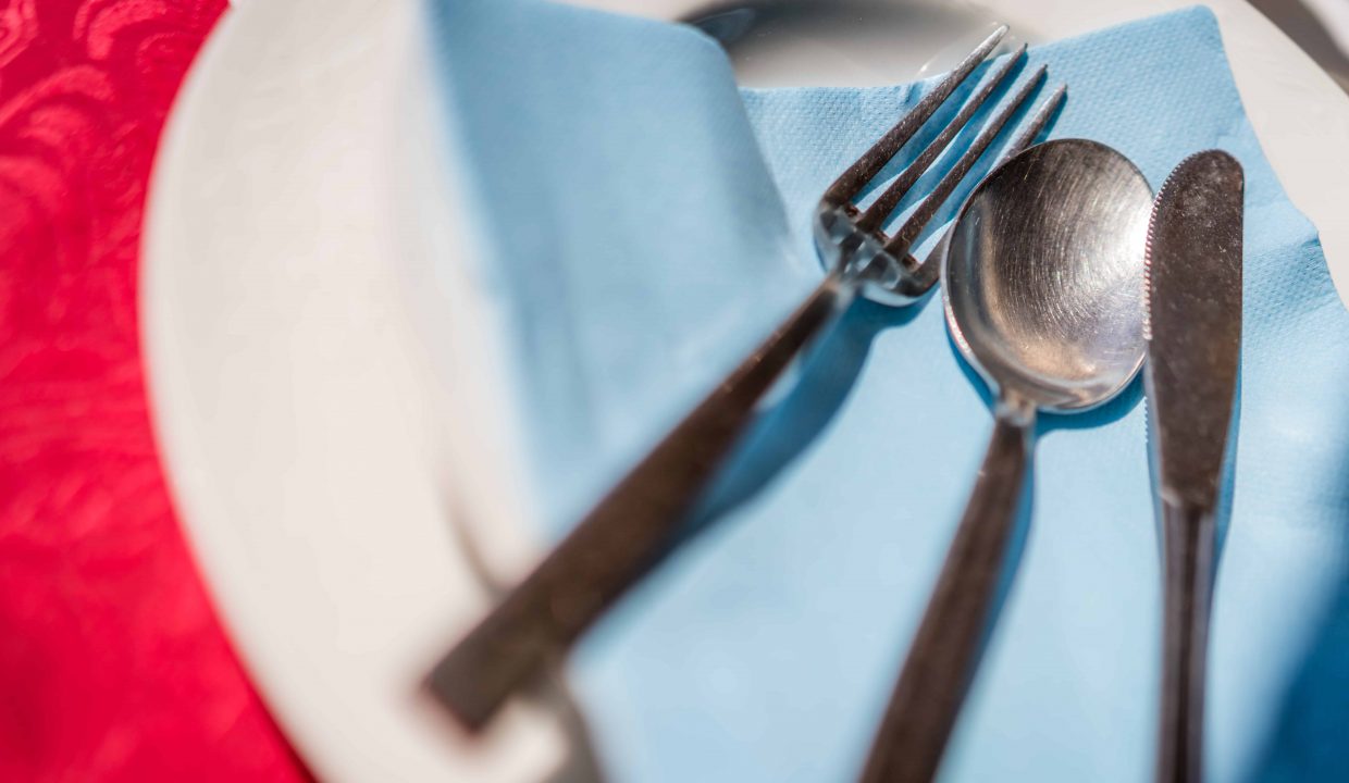 Fork, knife and spoon on a blue napkin on a plate on the table before the start of the service in the restaurant